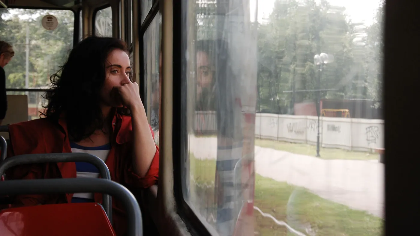 A woman riding a bus, resting her chin on her hand and looking out the window in thought